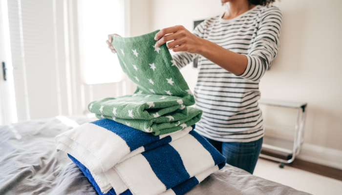Woman in striped shirt folding towels on bed.
