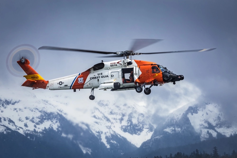 USCG Air Station Sitka Coast Guard orange and white helicopter hovering above snowy mountains