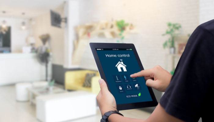 Person in black t-shirt holds up tablet displaying smart home app inside room in home.