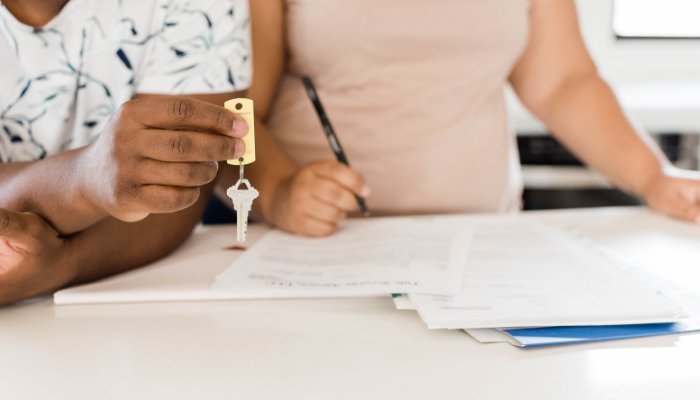 Picture of man and woman (chest down) standing at counter signing lease paperwork with house key in hand.