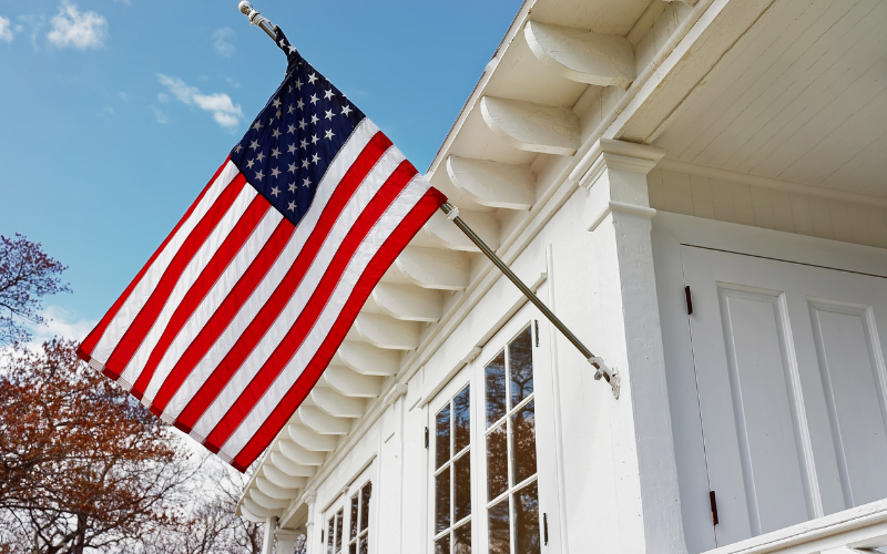 White home with detailed trim, large windows, and an American flag hanging.