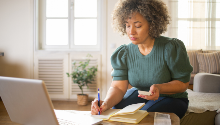 Woman in a short sleeve green top doing taxes with pen, paper, and calculator in front of the computer.