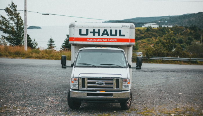 UHaul truck sitting on pavement with misty ocean and evergreens covering the hills behind.