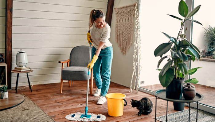 Woman smiling at cat while mopping wood floors with yellow bucket.