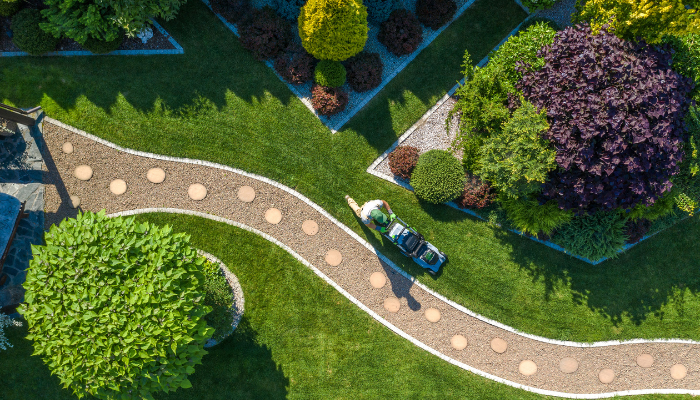 Aerial view of landscaped yard and pathway with person mowing. 