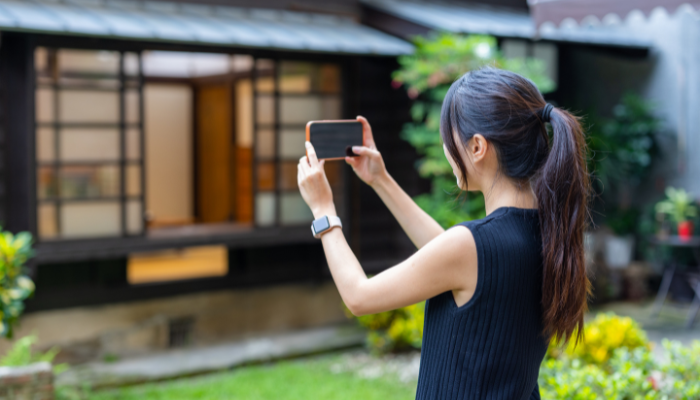 Woman taking photos of home exterior with phone.