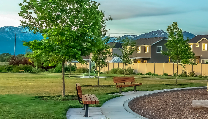 Edge of community area/playground in neighborhood with housing fences, trees, green field, and mountains in the background.