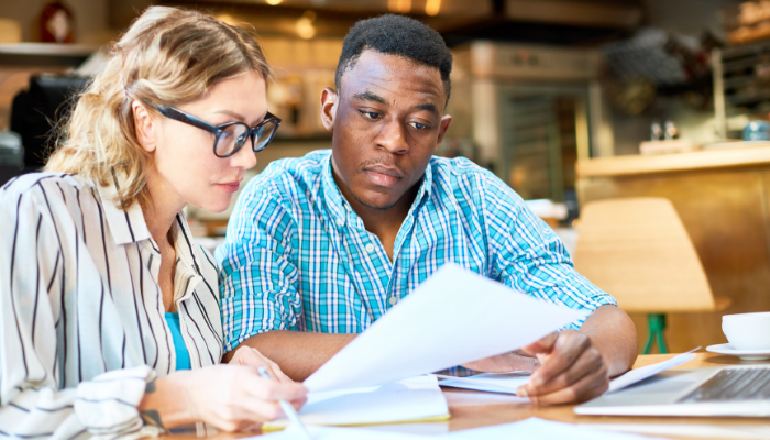Man and woman wearing button-downs at table looking over paperwork in front of them.