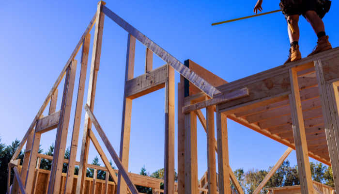Man standing on braces on new construction home site with blue sky.