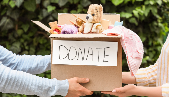 Two people wearing long sleeve shirt passing box of toys and clothing labeled "DONATE"