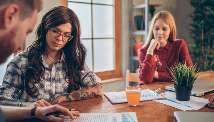 Two women and a man meet at table looking at paperwork.