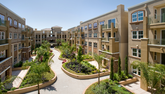 Stucco apartment complex with pathways lined in green landscaping.