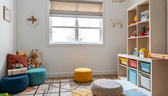 White-walled children's playroom with colorful accessories and brightly colored bins, poofs, and toys.