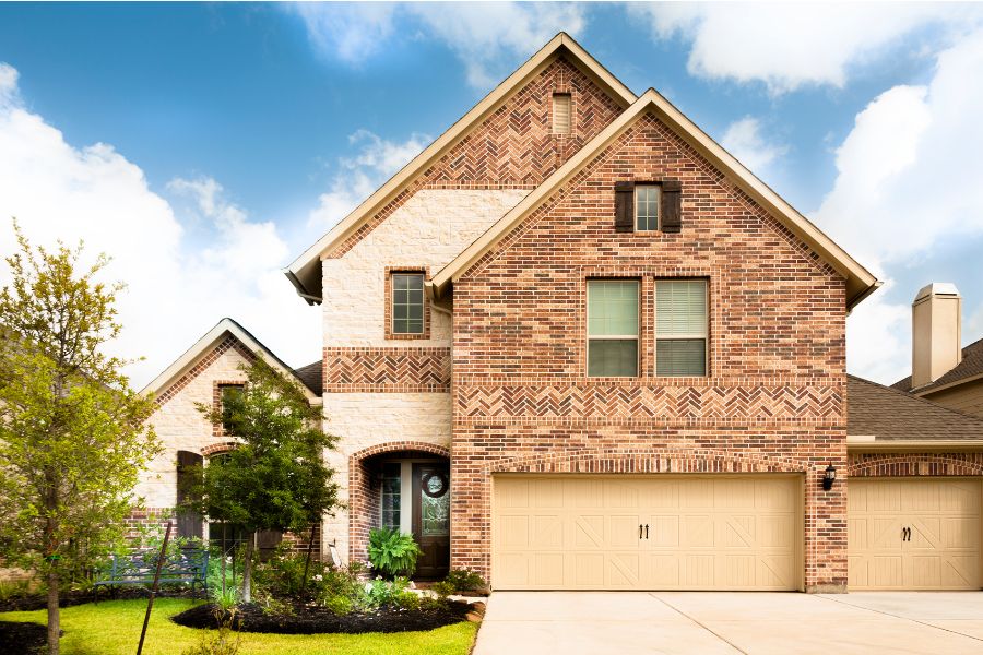 brown brick home with triple garage and trees with blue sky