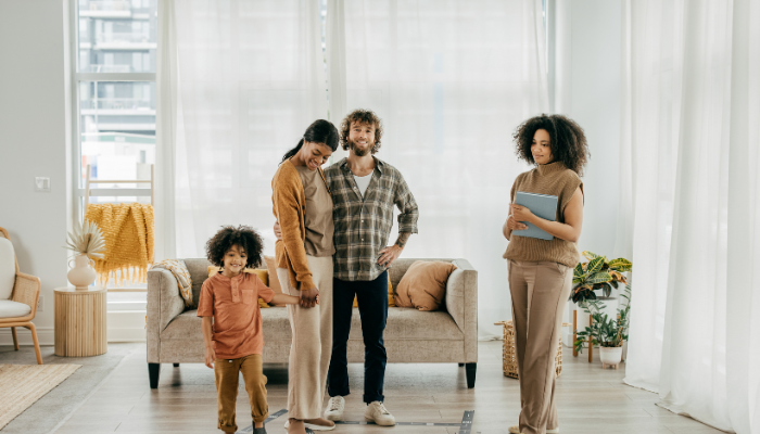 Man and woman with little boy in fall clothes mee with real estate agent in tan standing in living room. 