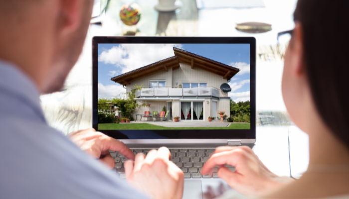View from behind of couple sitting next to each other looking at real estate listings on laptop.
