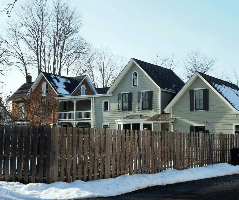 Two story home painted green with brown fence and snow on the ground