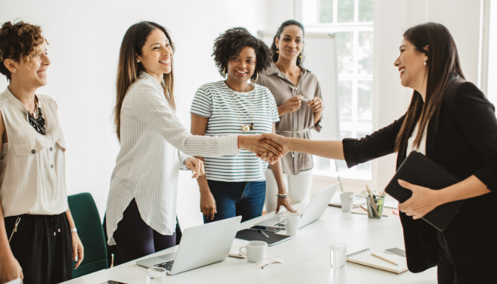Women at job fair meeting with potential employer, women standing around white table and shaking hands