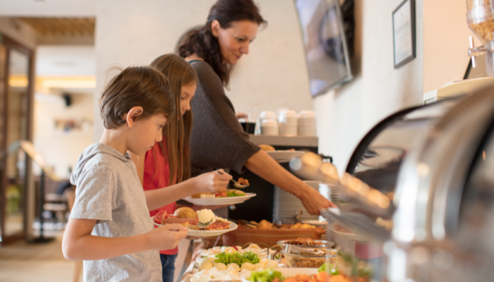 Mom and two children reaching food to fill their plates at hotel continental breakfast.