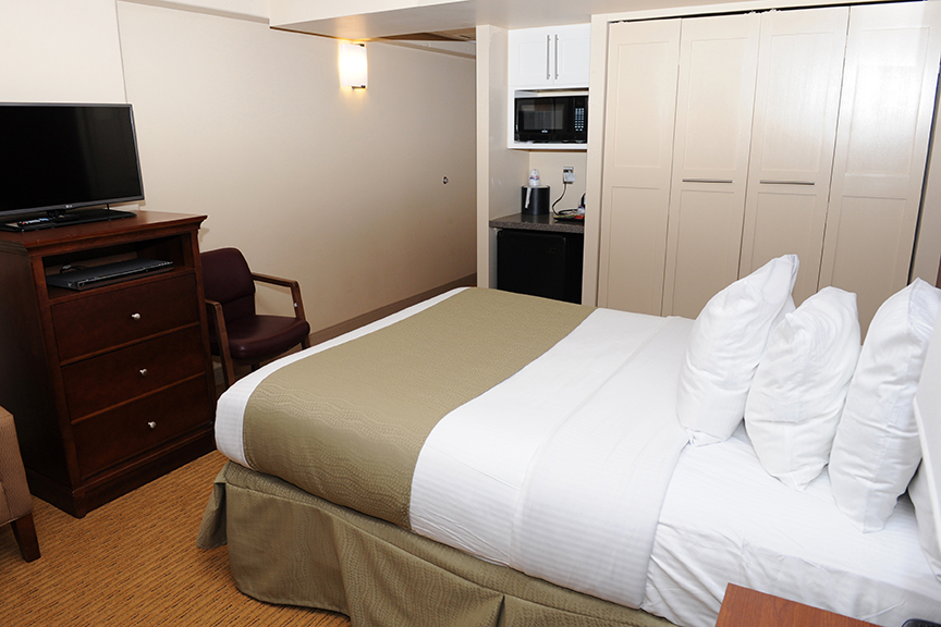 single bed with pillows, dresser, tv, nightstand, and small microwave and closet in military lodging room