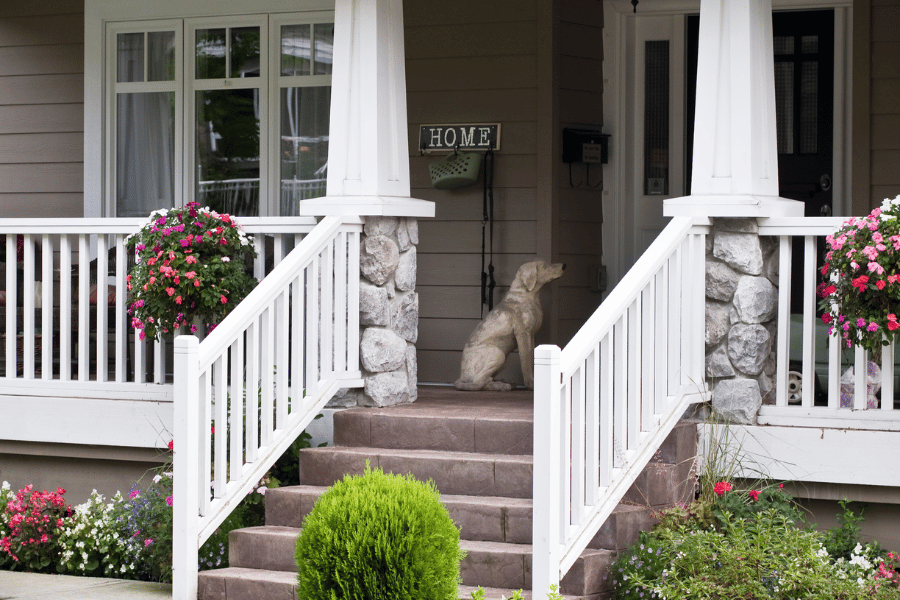 traditional style home with front porch and white railing, flowers, and green bushes