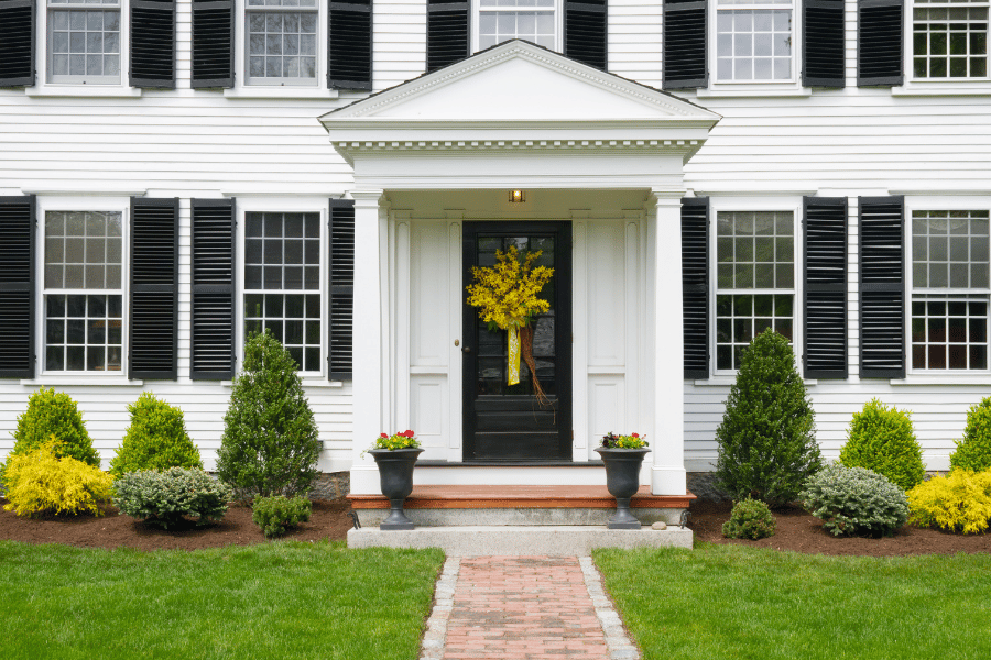 White two story home with black shutters and front door. Green grass and shrubs