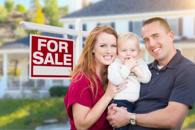 family in front of home with for sale sign