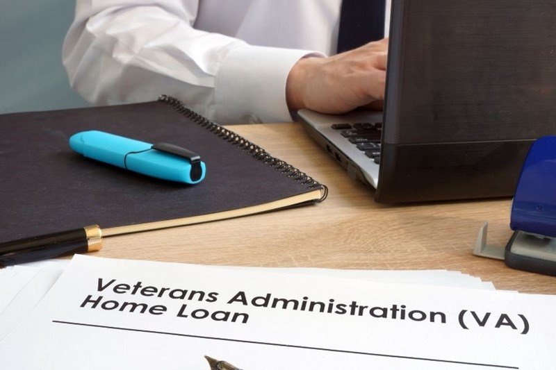VA home loan paperwork with real estate agent at laptop