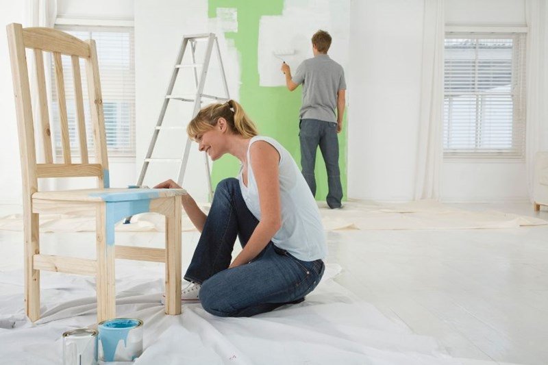 man and woman painting chair and wall of home