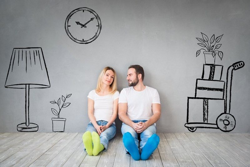 couple sitting against wall with drawings of furniture 