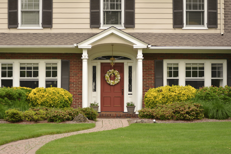 front of brick colonial home with wreath on door and green lawn and bushes