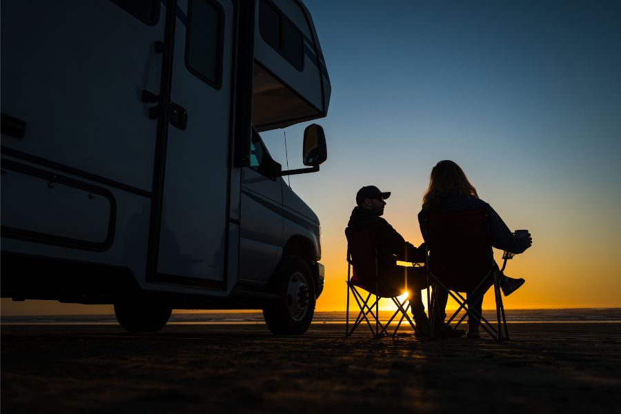 couple sitting in chairs outside RV at sunset