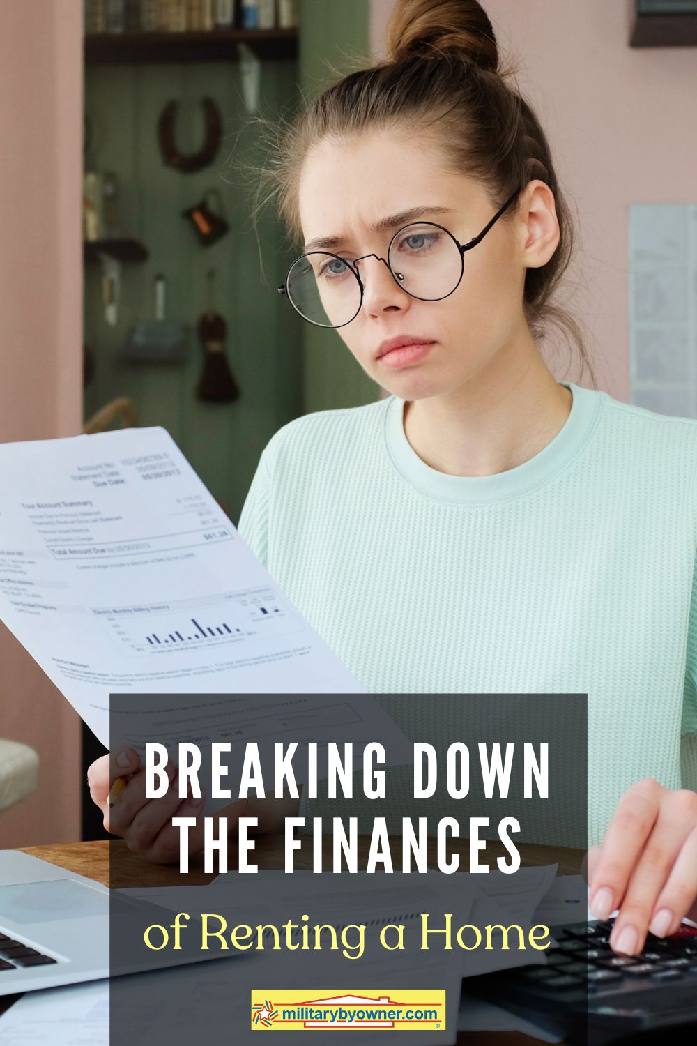 Woman with hair up in a bun wearing glasses concentrates on paper she's holding in front of computer and calculator with text, Breaking Down the Finances of Renting a Home