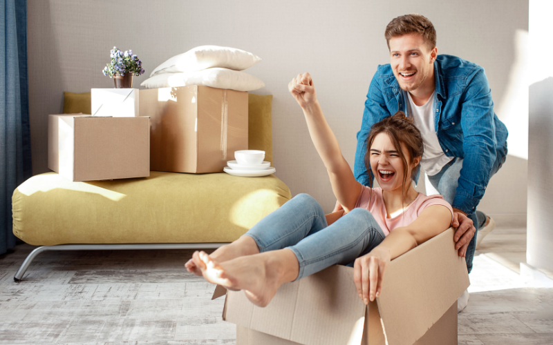 Man pushing happy woman in cardboard box while moving into house.