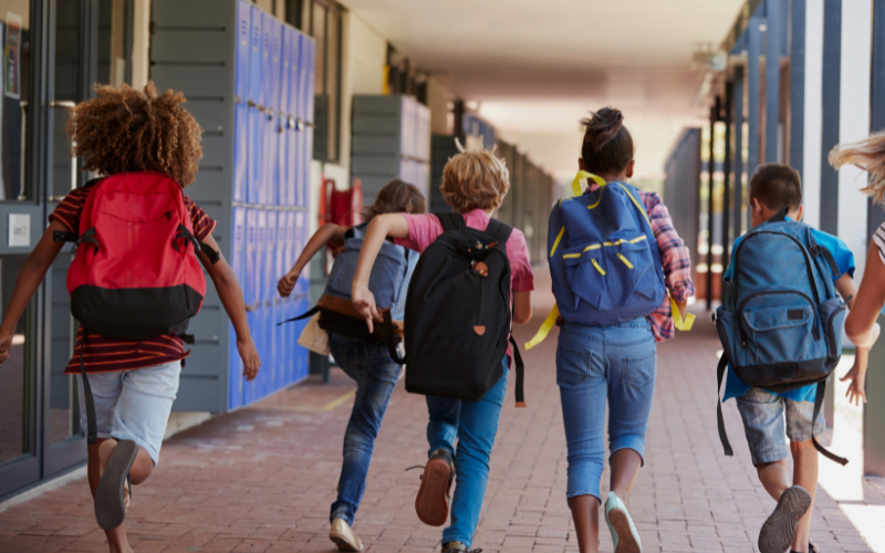 Line of kids running with their backpacks on through school hallway lined with blue lockers.