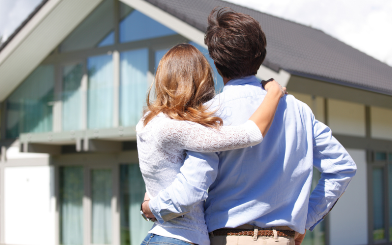 Couple with arms around each look at home to buy.
