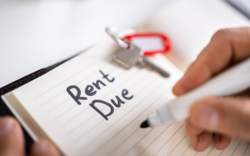 Person writing Rent Due in marker on notebook with key sitting nearby.