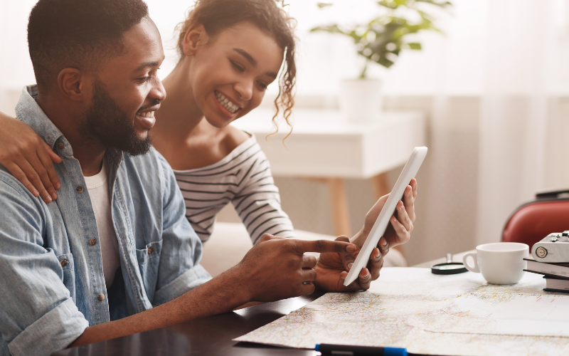 Couple smiling together while looking for a home to buy on tablet.