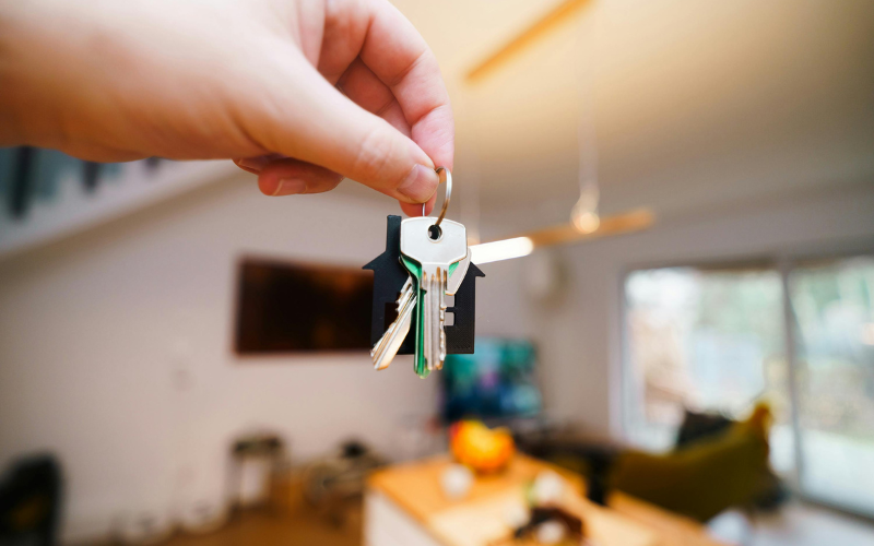 Person holding house keys in front of camera with room behind out of focus.