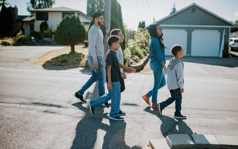Family of five, mom and dad with three boys walk through neighborhood street with sun casting shadows. 