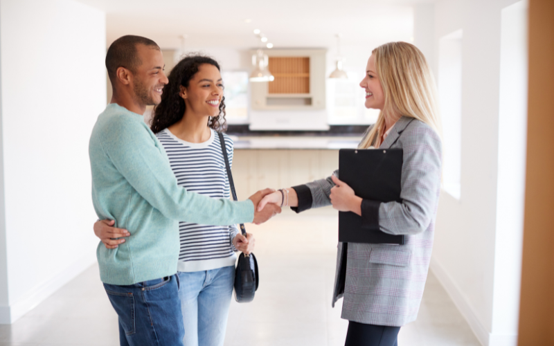 Couple shaking hands with a real estate agent in empty house.