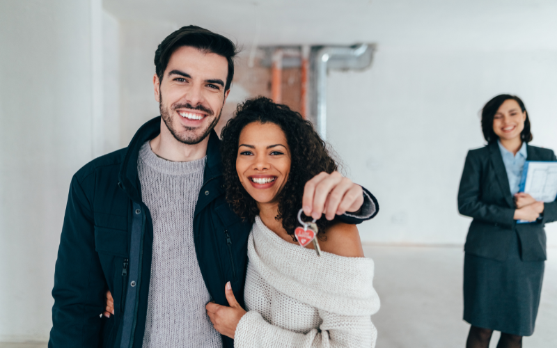 Smiling couple holding set of house keys with real estate professional behind them. 
