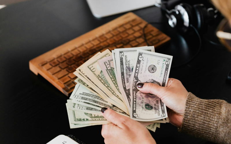 Person wearing long-sleeve sweater with fanned cash in hands.