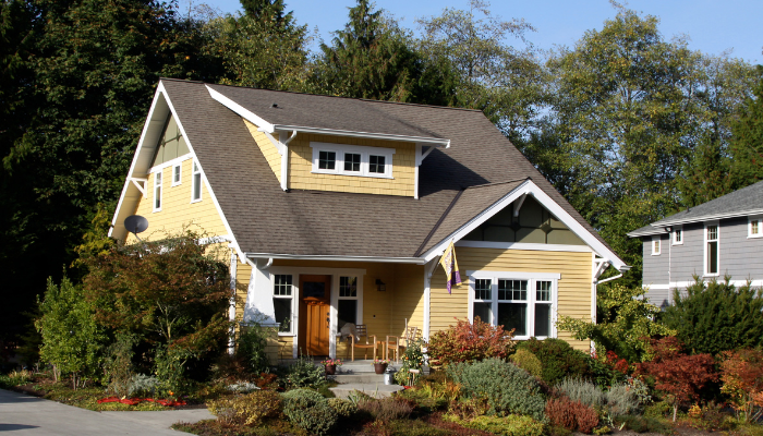 Yellow craftsman style home with white trim and large, mature landscaping surrounding.