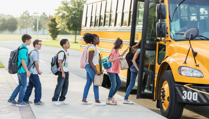 Line of kids in bright clothing filing onto yellow school bus.
