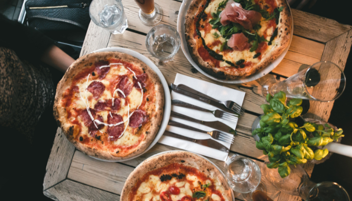 Aerial view of wooden restaurant table featuring gourmet pizzas with fresh basil on the table.