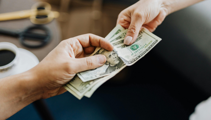 Two people passing handful of 20-dollar bills.
