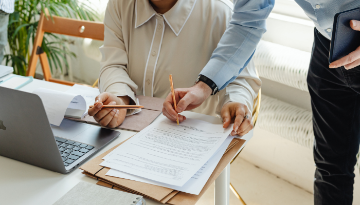 Man leaning over woman sitting with paperwork and computer.