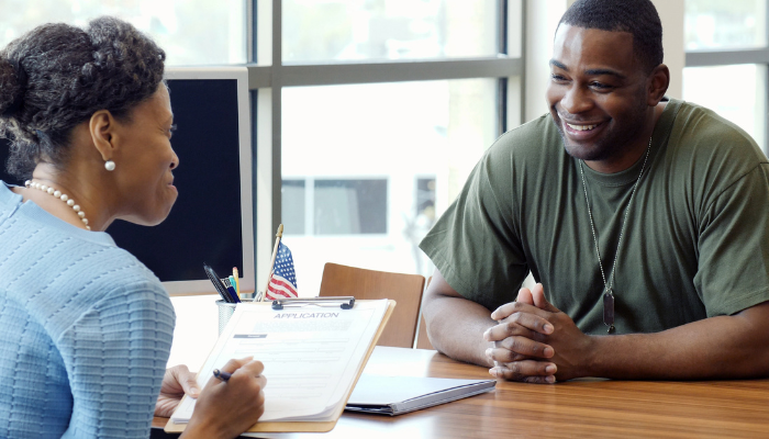 Man in green shirt smiles across desk at loan officer wearing blue with an American flag on her desk.