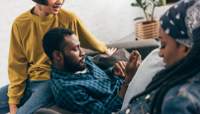 Photo of man and two women relaxing on couch while scrolling phone
